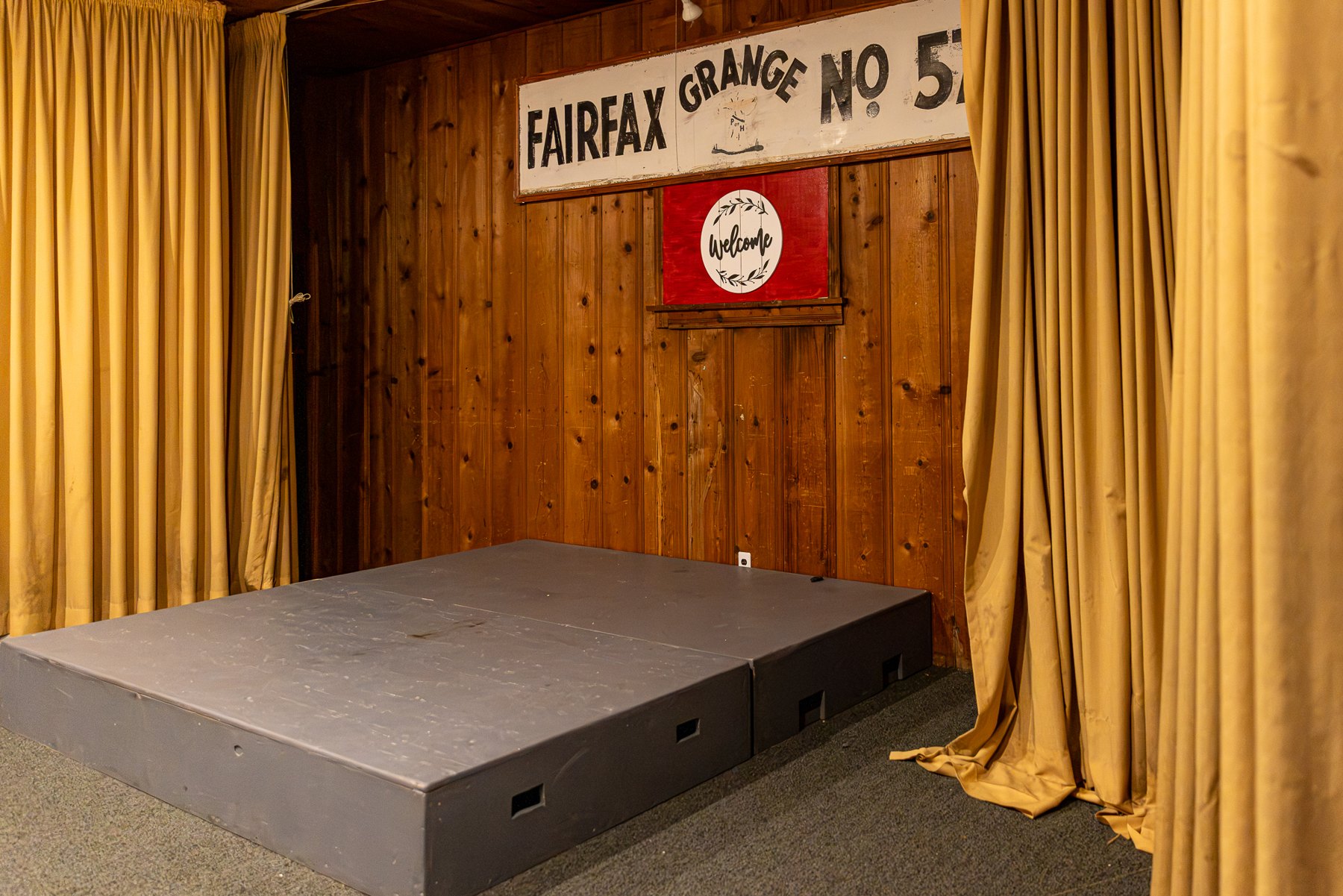 Raised stage with gold curtains and knotty pine backdrop at Fairfax Grange